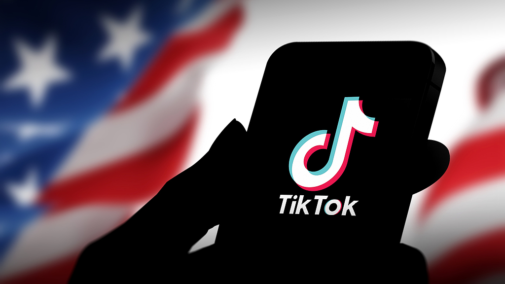 Le logo de Tiktok est vu sur un smartphone tenu devant un drapeau américain. / VCG