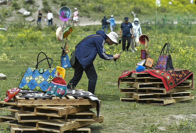 Un touriste prend des photos de la broderie kazakh dans un parc à Urumqi, la capitale de la région autonome du Xinjiang Uygur du nord-ouest, le 15 juin 2024. / VCG