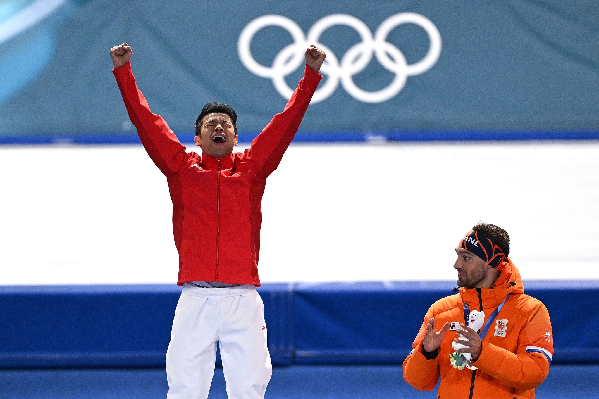 Ning Zhongyan (L), médaillé d'or de Chine, saute à côté du médaillé de bronze des Pays-Bas, Kjeld Nuis, sur le podium du 1 500 m masculin de patinage de vitesse lors des Jeux Olympiques d'hiver de Milano Cortina au stade de patinage de vitesse de Milan, en Italie, le 19 février 2026. /VCG
