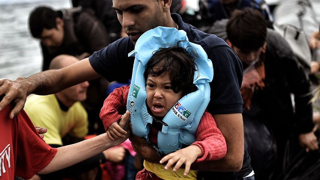 Un homme porte un enfant alors que les réfugiés et les migrants arrivent sur un canot sur l'île de Lesbos, en Grèce, le 30 septembre 2015. /VCG