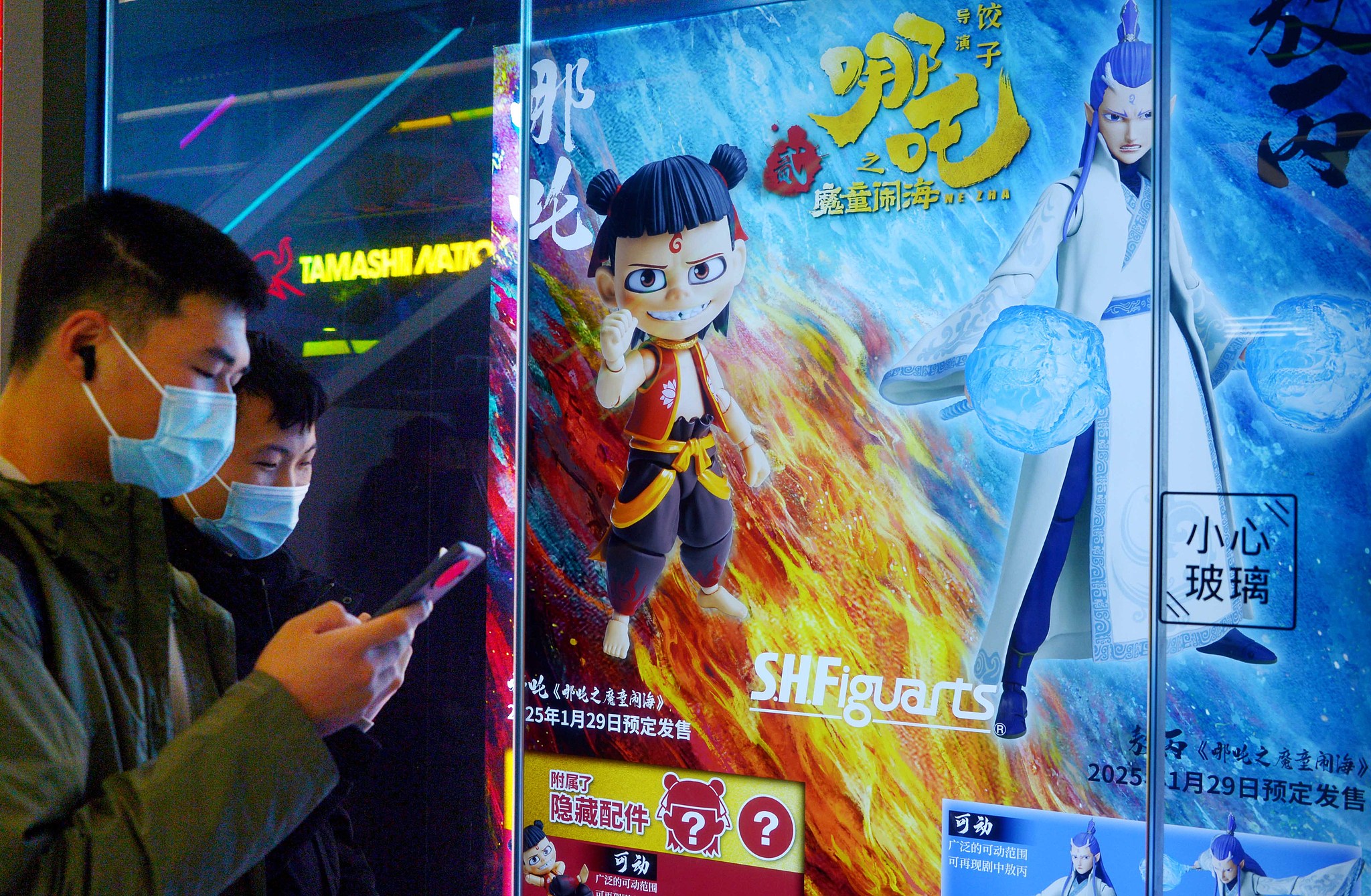 De jeunes visiteurs se tiennent devant une affiche de Ne Zha et parcourent des informations sur les produits liés au cinéma, Shanghai, Chine. /VCG