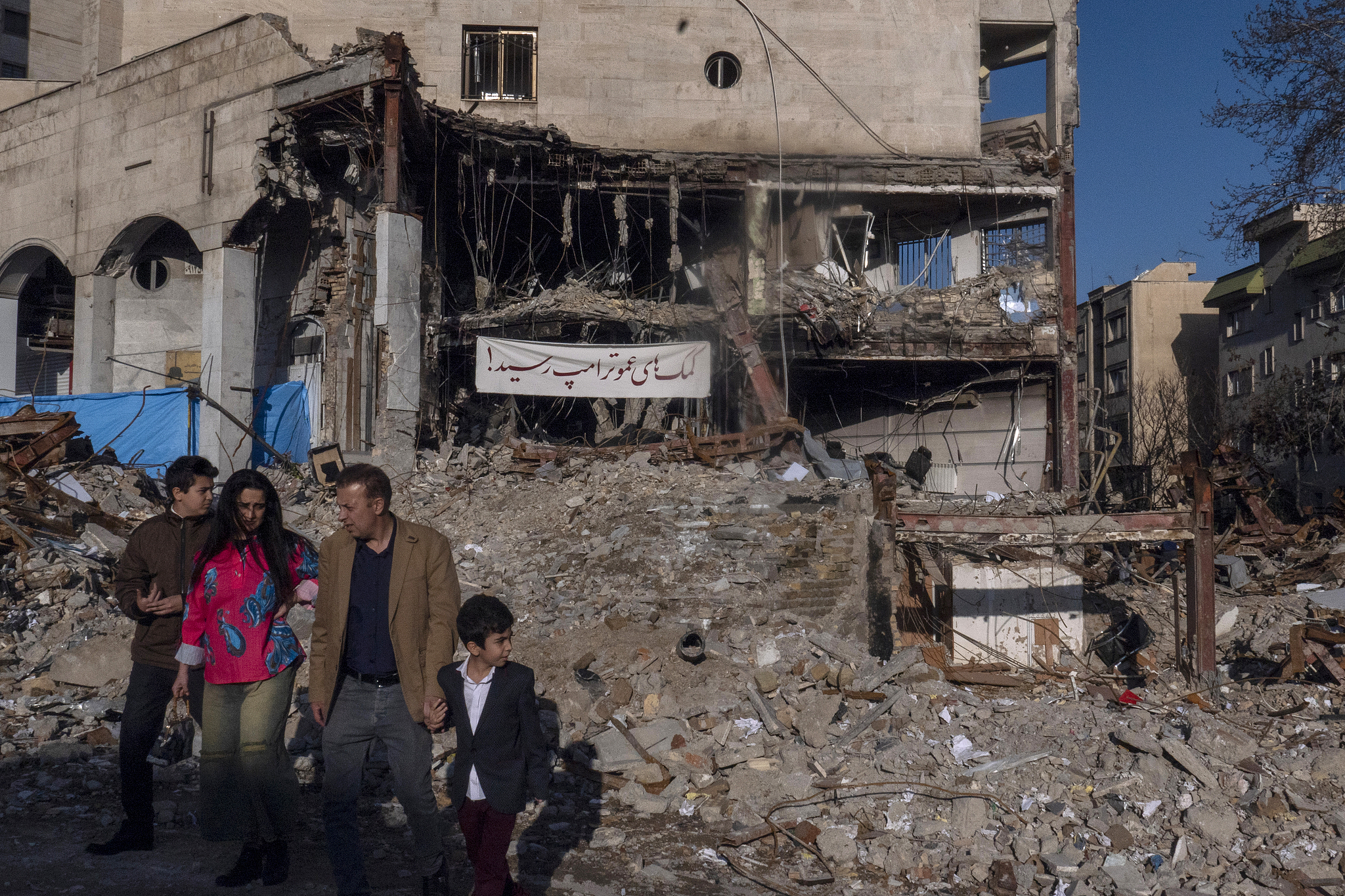 Une famille passe devant un immeuble résidentiel et commercial dévasté dans le quartier de Shahrak-e Gharb à Téhéran, en Iran, le 21 mars 2026. /CFP