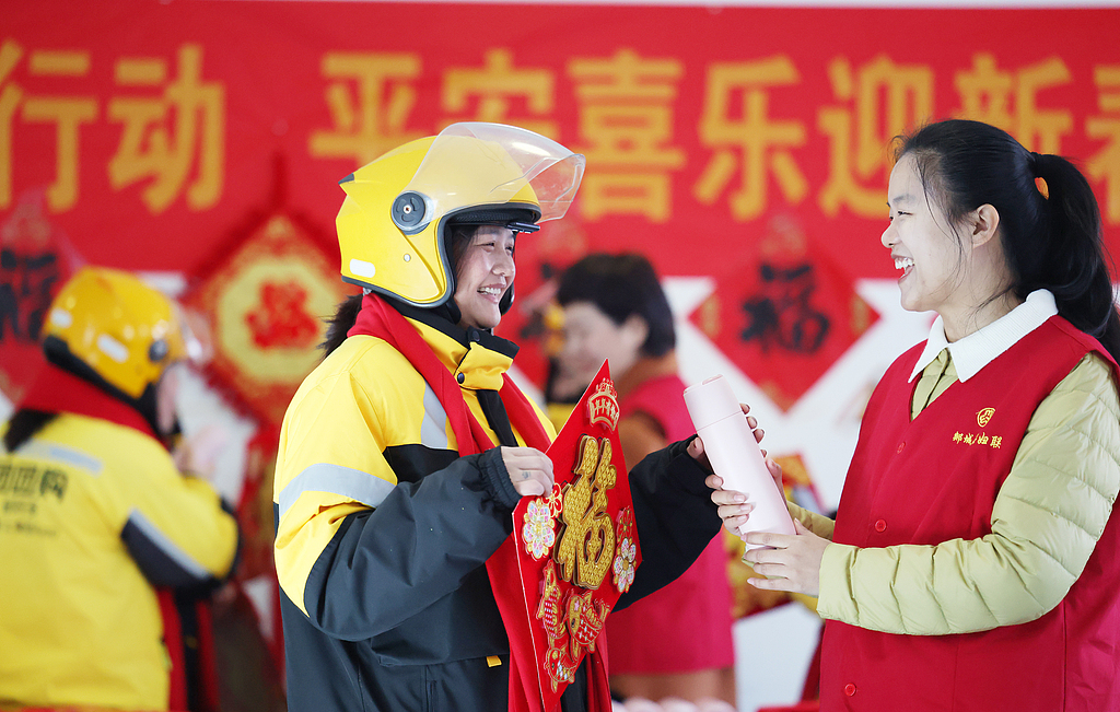 Des bénévoles de la Fédération des femmes présentent des foulards, des personnages Fu festifs et des tasses d'eau à des livreuses, dans la ville de Linyi, dans la province du Shandong (est de la Chine), le 9 février 2026. /VCG
