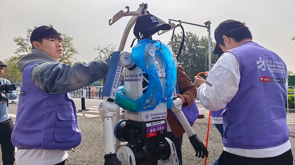 Les membres de l'équipe effectuent la maintenance de leurs robots dans une station de ravitaillement de robots lors du semi-marathon de robots humanoïdes 2026 à Pékin, en Chine, le 19 avril 2026. /VCG