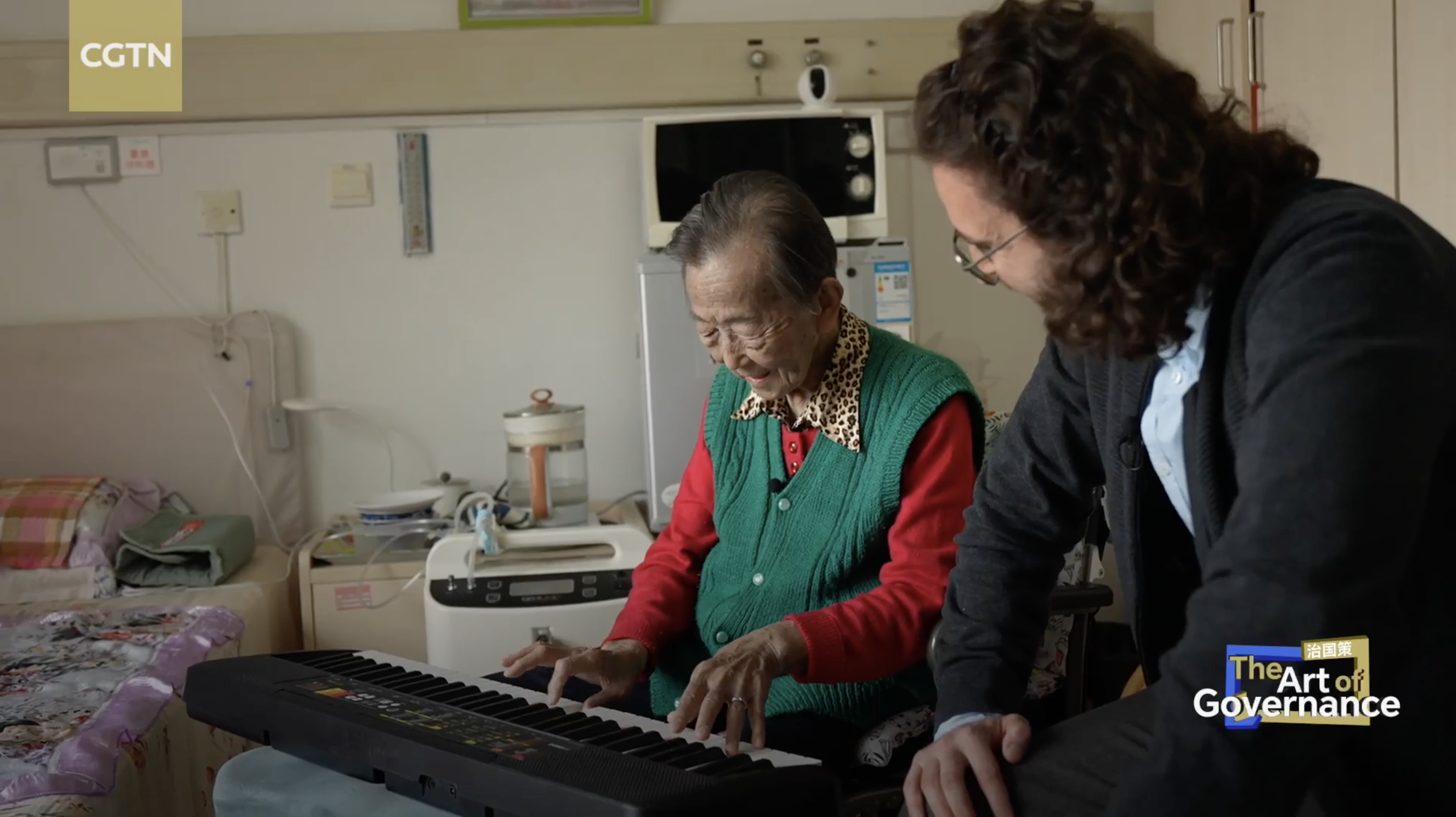 Yu Suqin, un habitant de 88 ans du district de Xicheng à Pékin, joue du piano dans sa chambre sous le regard du journaliste de CGTN, Nadim Diab. /CGTN