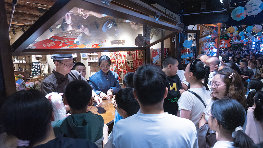 Des gens se rassemblent devant un stand donnant un spectacle interactif dans une rue historique du comté de Yilong, dans la province du Sichuan (sud-ouest de la Chine), le 2 mai 2026. /VCG