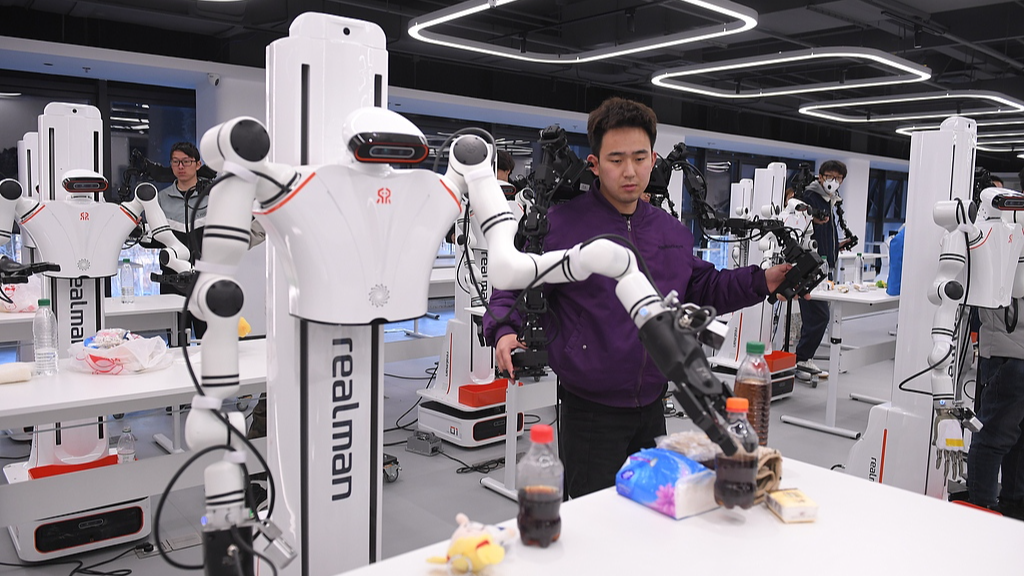 Des formateurs enseignent aux robots comment saisir et ramasser une bouteille dans un centre de formation aux données sur les robots humanoïdes du district de Shijingshan à Pékin, en Chine, le 28 mars 2025. /VCG