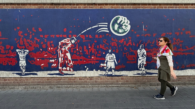 Une femme passe devant une fresque représentant le milieu de terrain iranien Hamid Estili marquant contre les États-Unis lors de leur match de Coupe du Monde de la FIFA 1998, que l'Iran a remporté 2-1, sur le mur de l'ancienne ambassade américaine, aujourd'hui musée, à Téhéran, Iran, le 12 juin 2026. /VCG