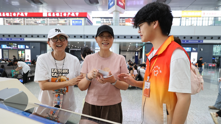 Une jeune bénévole aide des femmes âgées à acheter des billets dans une gare de la municipalité de Chongqing, dans le sud-ouest de la Chine, le 23 juillet 2026. /VCG