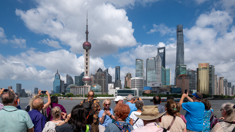 Des touristes étrangers prennent des photos sur la plate-forme du front de mer du Bund avec en toile de fond la ligne d'horizon de Lujiazui à Shanghai, le 10 juillet 2026. /VCG