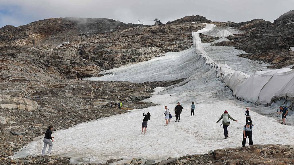 Des gens marchent à côté d'une polaire de protection recouvrant une partie du glacier du Moelltal en Carinthie, en Autriche, le 19 août 2026, alors que le glacier s'est rétréci en une étroite bande de neige au milieu d'une perte de glace accélérée à travers les Alpes, où la superficie du glacier a chuté de 39 % depuis 2000. /VCG