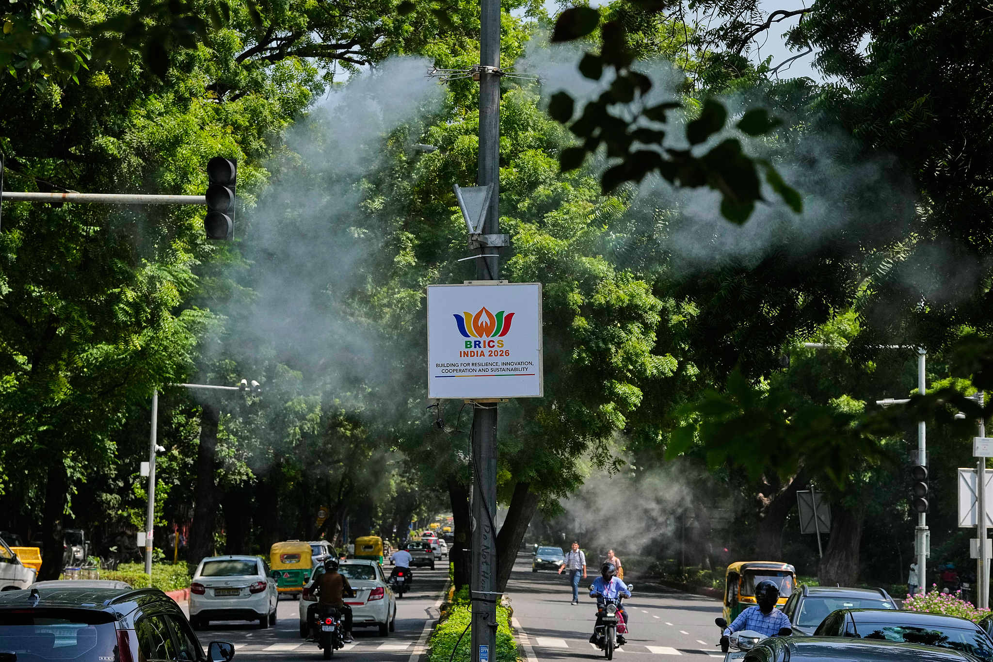 Des jets d'eau pulvérisent du brouillard pour supprimer la poussière des routes et aider à réduire la pollution de l'air alors qu'une bannière du sommet des BRICS est suspendue à un poteau électrique à New Delhi, en Inde, le 10 septembre 2026. /VCG