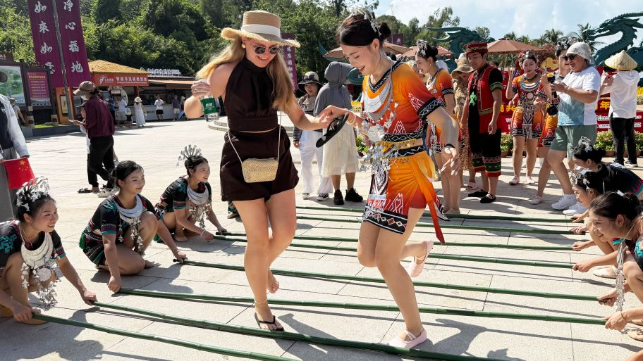 Un touriste étranger s'essaye à la danse à la perche en bambou dans une zone pittoresque de Sanya, dans la province chinoise de Hainan (sud), le 1er octobre 2026. /Xinhua