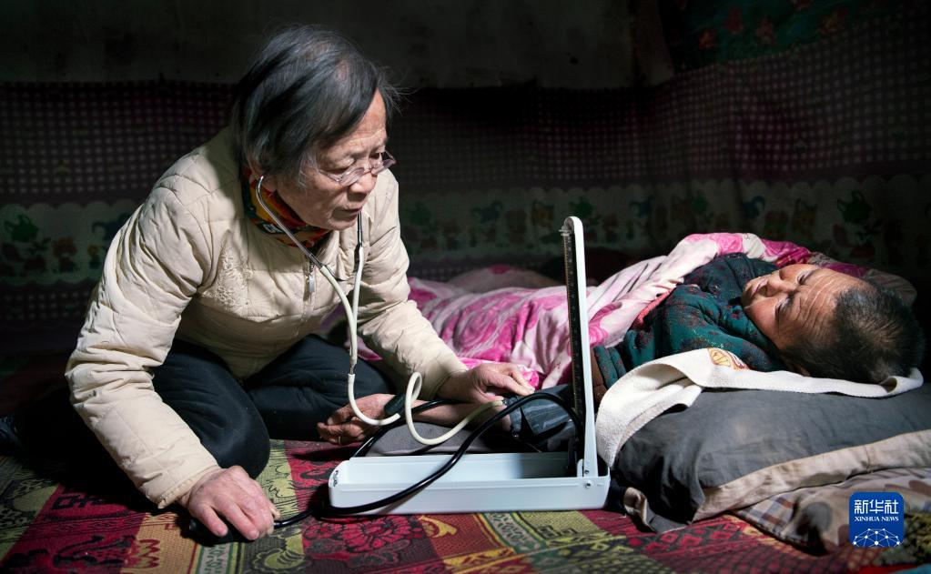 Lu Shengmei (à gauche) s'agenouille sur un lit kang en terre traditionnel pour offrir une consultation médicale gratuite à la villageoise paralysée Qiao Aifen dans sa grotte du village de Hejiagou, ville de Dian, comté de Jiaxian, province du Shaanxi, le 18 janvier 2021. /Xinhua