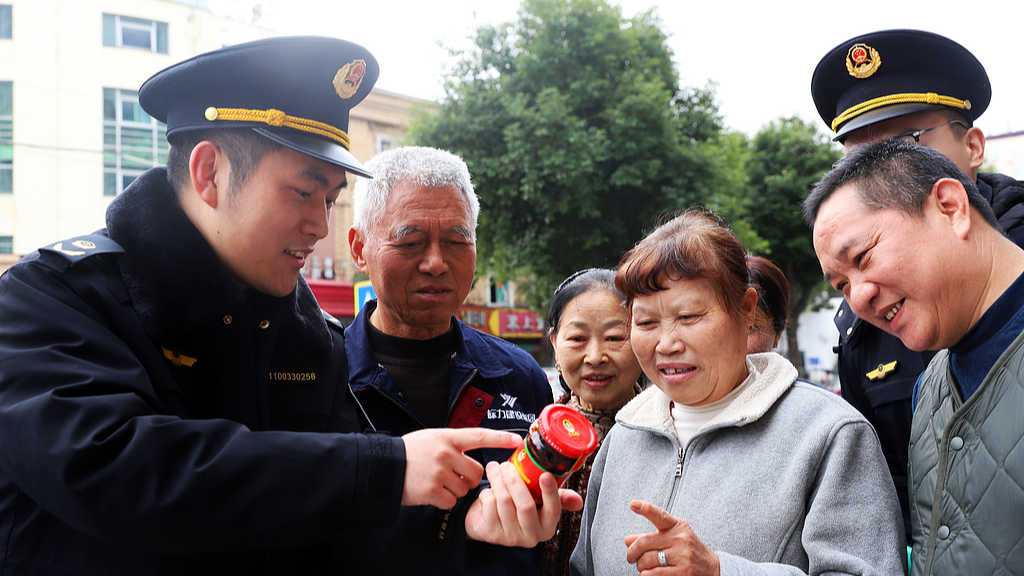 Un responsable des autorités locales de régulation du marché explique aux résidents locaux comment identifier les produits contrefaits dans la ville de Taizhou, province du Zhejiang (est de la Chine), le 9 mars 2026. /VCG