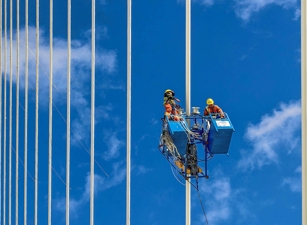 Des ouvriers enveloppent les haubans pour les protéger contre la corrosion sur le grand pont de Yongjiang à Ningbo, province du Zhejiang, Chine, le 25 juillet 2026. /VCG